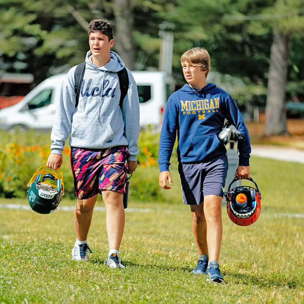 Two campers holding football helmets on their way to practice.